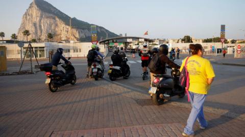 People on foot and motorbikes cross the border from Spain to Gibraltar at dawn, in front of the Rock
