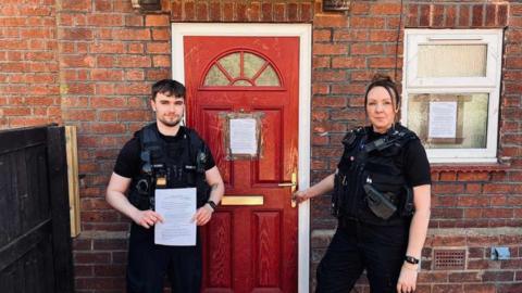 Two police officers stood in front of a red door.