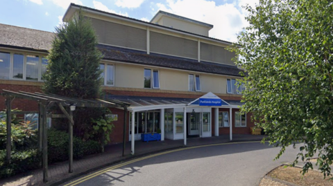 Parklands Hospital is a red brick and cream render building with two floors and a tiled roof. It is seen from outside and includes a white canopy entrance with a hospital sign above the door