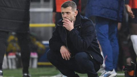 Jack Wilshere crouches down and strokes his chin in technical area
