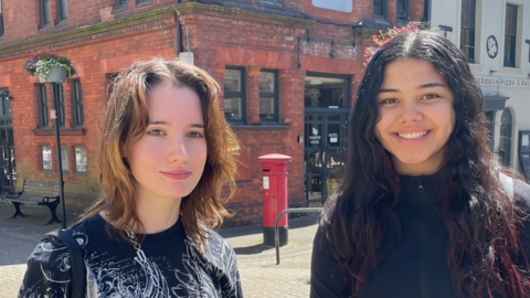 Two young women on a sunny street, looking directly at the camera