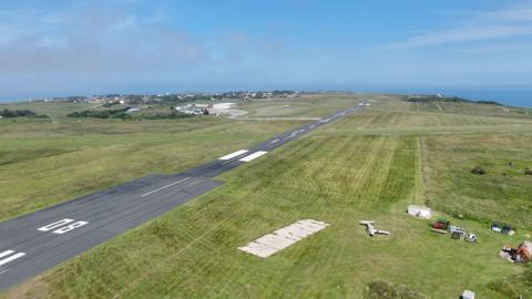 Aerial view of Alderney Aiport. The runway is located between two large green spaces. 