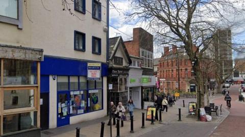 Shoppers walk past the empty blue betting shop that will soon be turned into a homeless centre