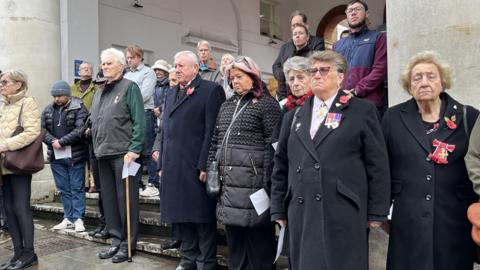 Crowds of people some with medals lower heads and mark silence in Guildford.