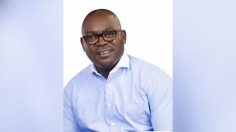 Mutotwe Kafwaya in black-rimmed glasses and a blue shirt
