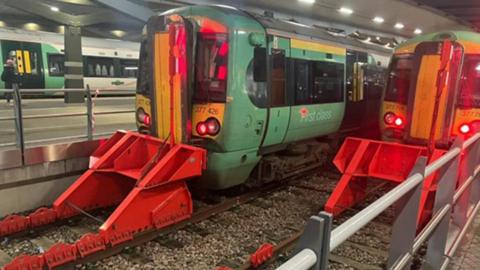 Green train in contact with red buffer at platform. Red lights can be seen