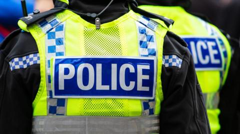 Police officers wearing black jackets and yellow his vis vests with blue and white writing that reads: Police