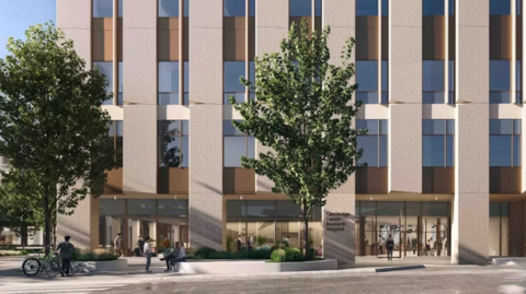 A CGI image of what the new cancer hospital will look like.It is tall and has different brown blocks and panels on its front, as well as many windows. There is a tree in front of the building and people are sat or walking around.