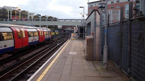 Platform at Stratford shows Jubilee line train on left with bridge ahead and housing in the background