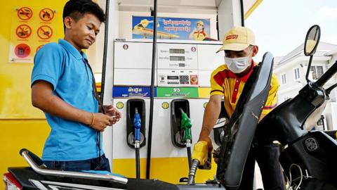 An employee pumps fuel into a motorbike as a customer his right watches
