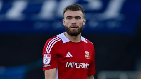 Aaron Drinan standing on the pitch during a match for Swindon with his arms by his sides