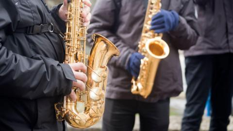 Two young men playing saxophone outdoors, marching band in a traditional celebration