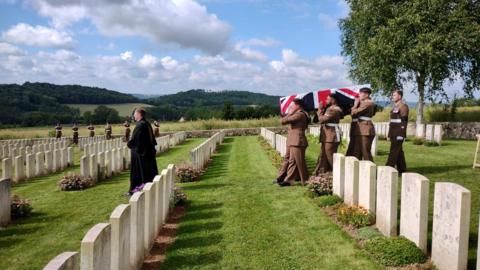 Members of the army bear a coffin draped in the Union Flag through a graveyard, led by a vicar