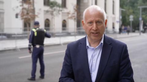 Russia editor Steve Rosenberg reporting from Russian street, with police officer seen behind him
