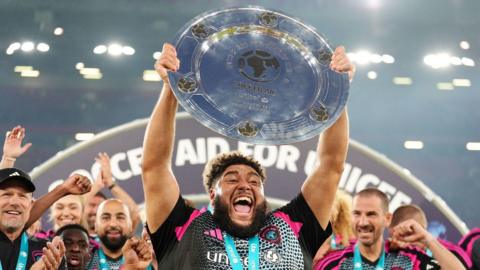 Big Zuu holding up Soccer Aid trophy. 