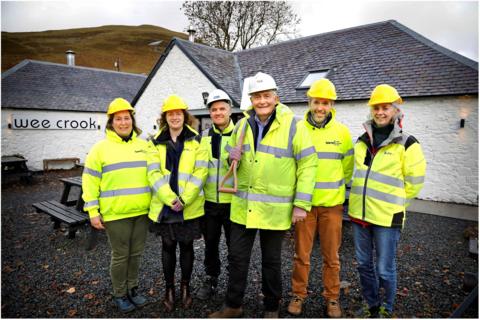 A line-up of six people in high visibility gear, one of them carrying a shovel, outside the Wee Crook cafe - a white building with a black slate roof