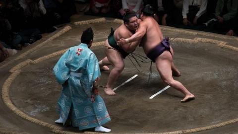 Two sumo wrestlers fight each other in a clay ring