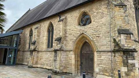 A stone chapel built from stone blocks with a steeply pitched slate roof, Gothic-style windows set into the wall and a pointed-arch doorway. 