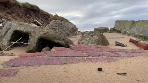 Remnants of a red brick wall sunken in sand and rocks