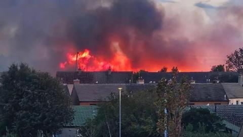 Flames and smoke rise above the roofs of nearby houses 