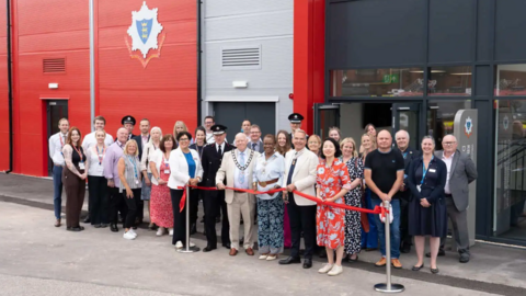 A large group of people, dressed smarty, standing outside the entrance of the new training centre. The building has red, silver and black walls and glass doors.