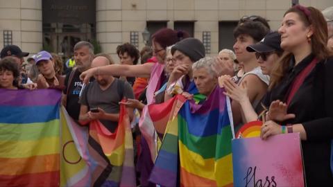 People standing in a line holding rainbow coloured flags