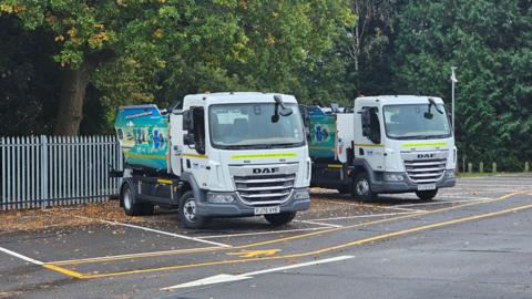 Two white lorries parked up in a car park with tippers on the back