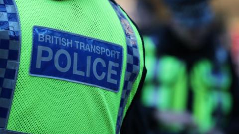 A close up image of a person's back. They are wearing a hi-vis vest which has a blue patch which says British Transport Police on it.