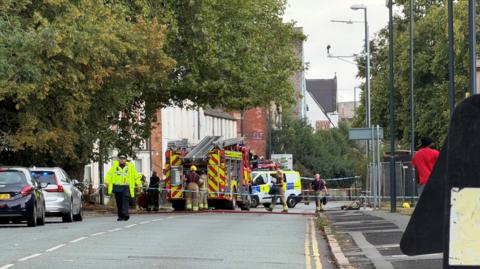 Police tape across a road with a fire engine and police car parked on the street