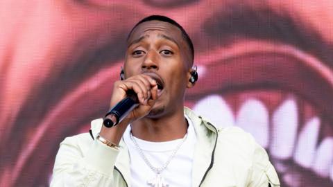 Yung Filly performing at the Parklife Festival in 2022. He is singing into the microphone and is wearing a white T-shirt and cream jacket.