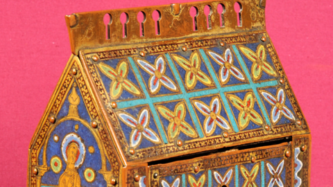 a small box decorated in medieval art with colours of blue, green, red and gold. It has a hand painted illustration of a male saint, st thomas becket 