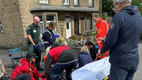 Paramedics and volunteers treat a man on the floor. They appear to be trying to place him on a stretcher.