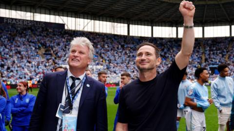 Coventry City owner Doug King pictured with manager Frank Lampard at the Coventry Building Society Arena celebrating with fans. They are both smiling and Frank Lampard has his left first raised in celebration.