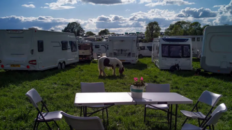 A field with a table and chairs in the foreground and a horse and caravans in the background. 