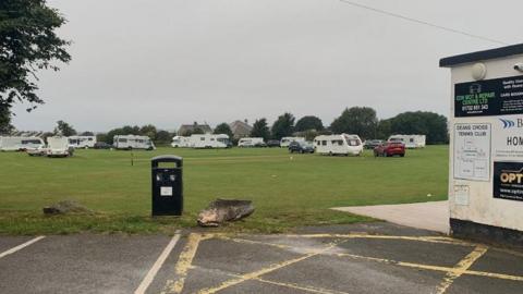 A picture of the vans parked on the large grass field. A number of vans can Be seen parked on the grass in the distance. 