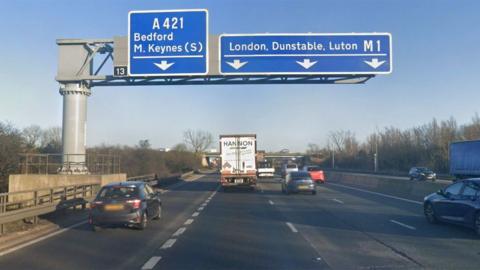The exit for junction 13 of the M1 southbound, showing four lanes of traffic and a big sign above the road showing the right three lanes for the M1 - and the inside lane for the A421.
