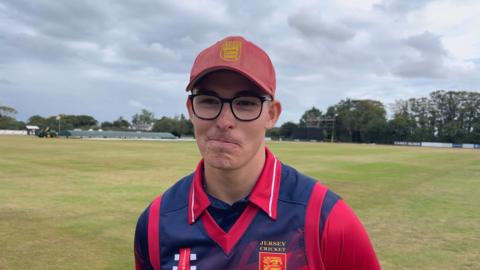 Cricketer Asa Tribe wearing black-rimmed glasses and a red baseball cap