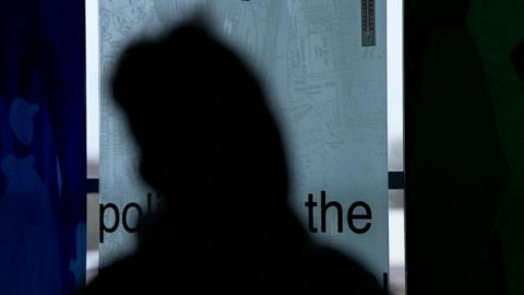 A silhouette of a woman in front of a police poster 