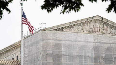 The exterior of the US Supreme Court with an American flag in foreground