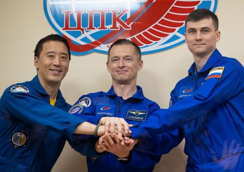 NASA astronaut Jonny Kim, left, and Roscosmos cosmonauts Sergey Ryzhikov and Alexey Zubritskiy seen in quarantine, behind glass, as they pose for a picture following a press conference.