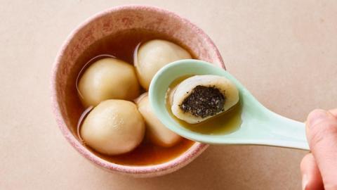 Black sesame tangyuan in a light pink bowl with one cut open on a spoon.