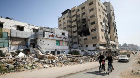 Palestinians ride bicycles past the war-damaged al-Basma IVF Centre in Gaza City, northern Gaza