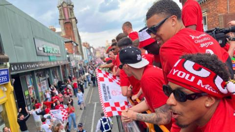 Lincoln City fans on top of an open top bus with cheering fans below