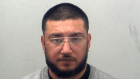 A man in a custody photo. He has a beard and glasses and has a beard. He is looking at the camera 