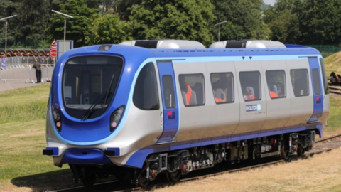 A blue and silver one-carriage train on a track running through a grassy area