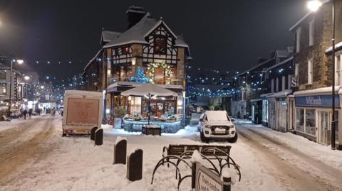 Snow covered town with lights strung up on a high street. 