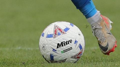 A National League football with HUFC written on it being kicked by a white boot and a blue sock