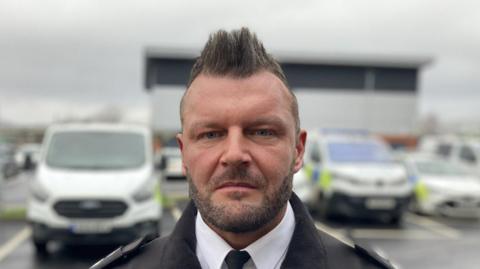 Temporary Chief Inspector Greg Owens. He has a dark short beard and his brown hair is styled-into a mohawk.
