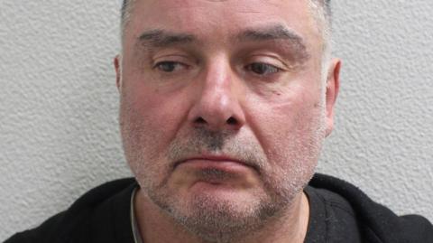 Custody image of Thomas McKenna, wearing a dark top, photographed against a plain wall.