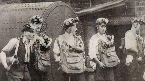 An old black and white photograph of men in mining gear.